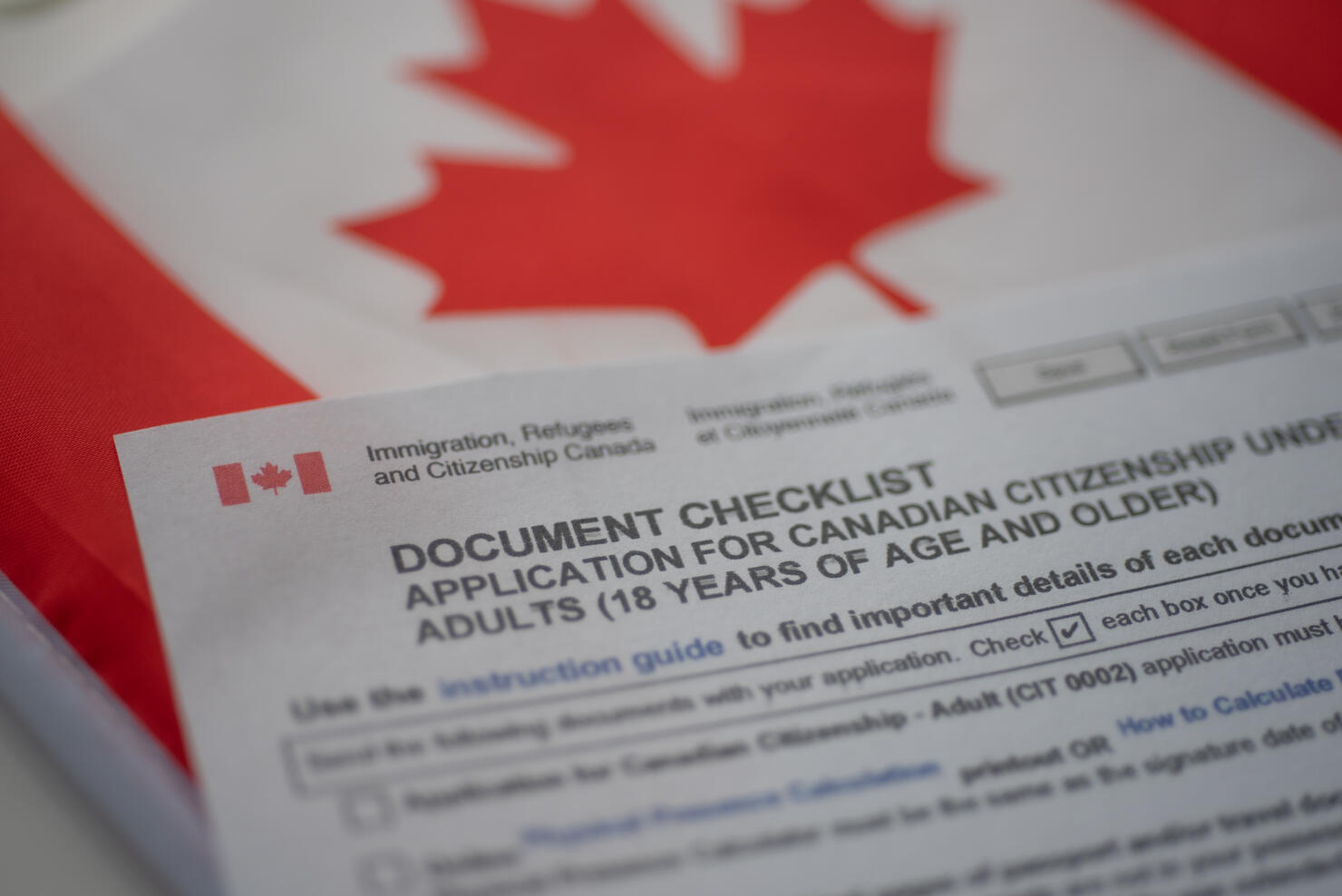 Document check list application for canadian citizenship next to Canadian flag, close up view.