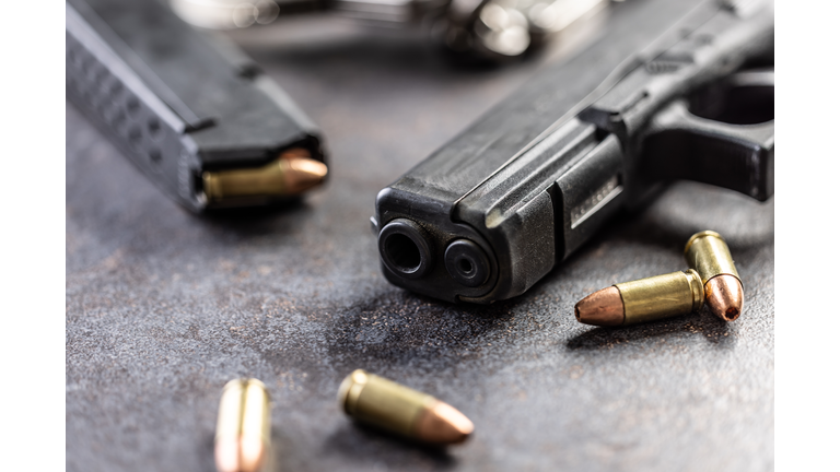 Close-up of a black metal 9mm automatic pistol with bullets all placed on a concrete table