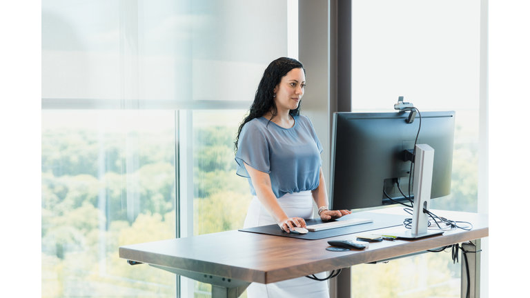 Using standing desk, female CEO works in corner office