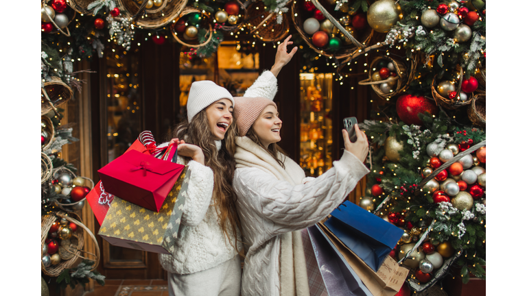 Beautiful happy girls holding shopping bags in hands and smiling standing near shopping mall.