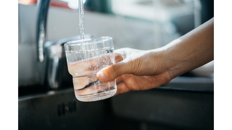 Close up of a woman's hand filling a glass of filtered water right from the tap in the kitchen sink at home