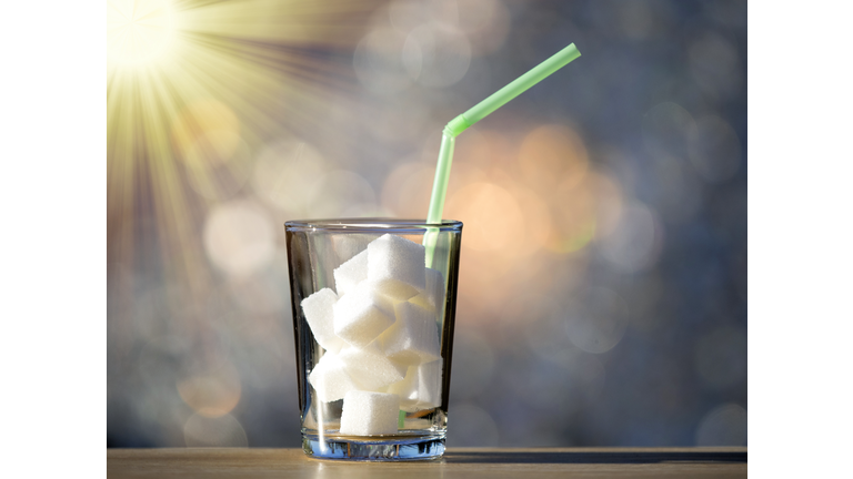 Crystal glass with nine lumps of sugar equivalent to the content in sugar of a refreshing drink illuminated by sunlight.