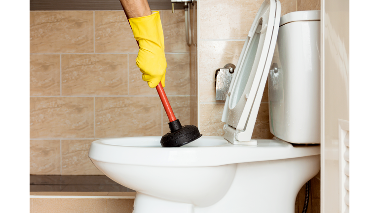 Human hand wearing yellow rubber gloves is using a device to fix a clogged toilet bowl.
