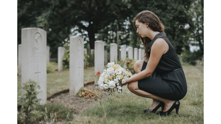 Young widow laying flowers at the grave