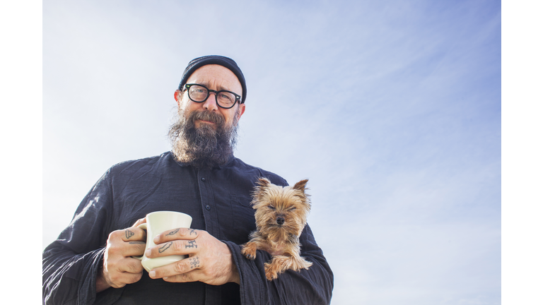 Bearded man holding small dog and coffee cup