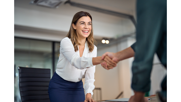 Happy mid aged business woman manager handshaking greeting client in office.