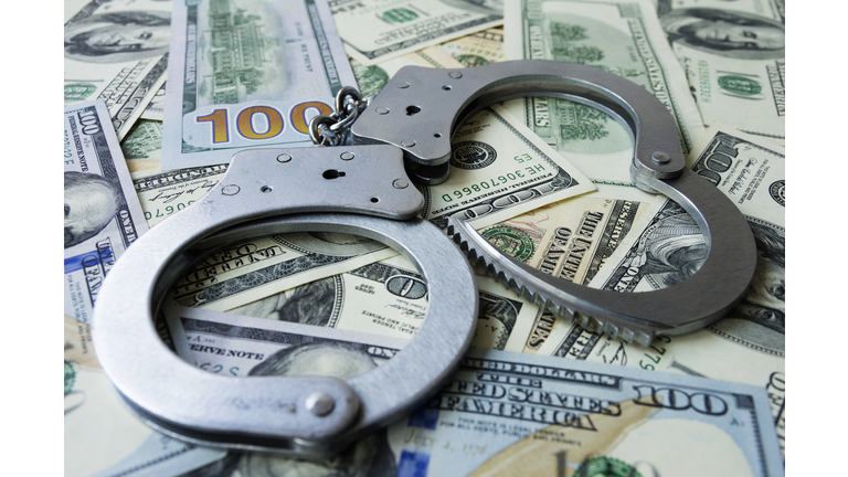 Handcuffs on a pile of US dollar banknotes- symbolic image of a bribe, laundering of money or corruption. Selective focus.