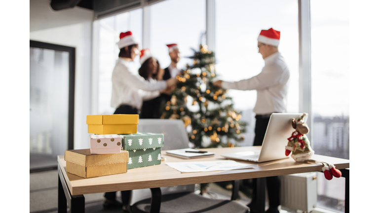 Focus on table with gifts of group of coworkers decorating christmas tree