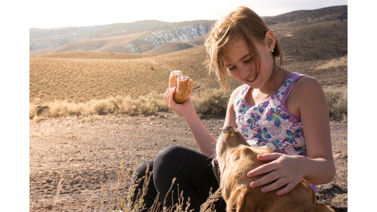 11 year old girl having a snack with her dog.