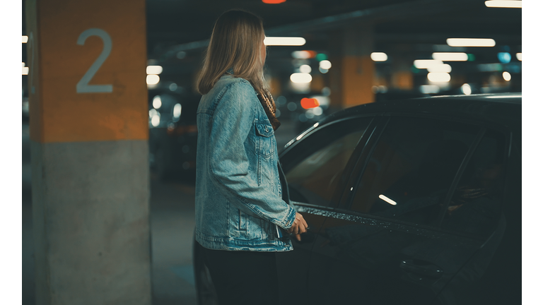 Woman unlocking her car with key in underground parking.