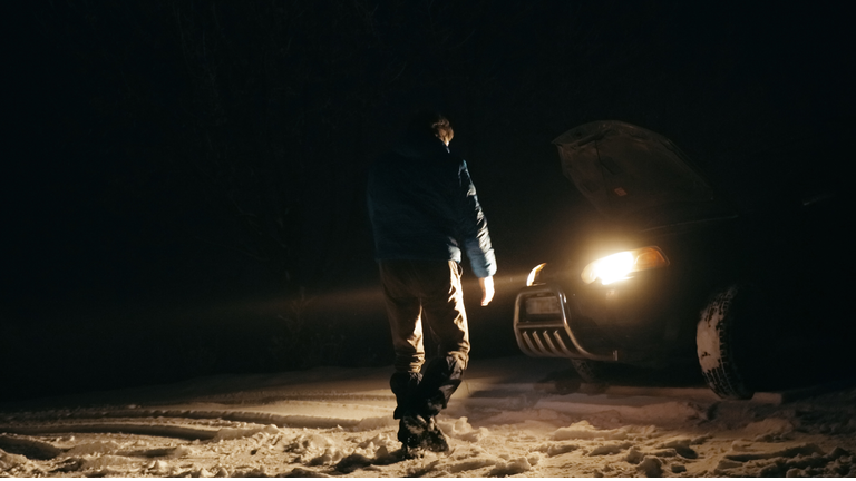 Man with car issues on winter road, phone calling for help.