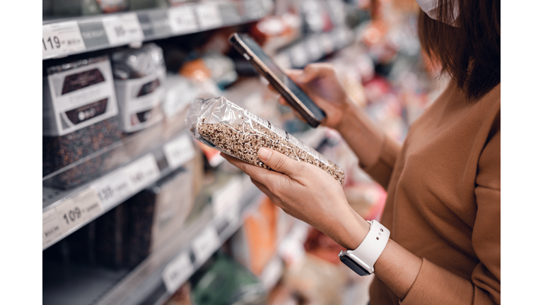 Woman shopping in supermarket and reading product information. Costumer buying food at the market.