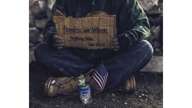 Fighting adversity. Homeless war veteran with sign and money tin