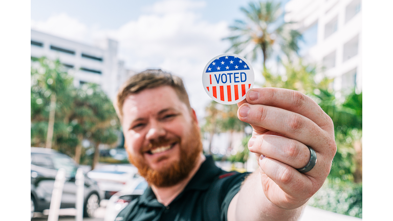 "I Voted" Sticker, held up to camera by Caucasian Man wearing a Wedding Ring