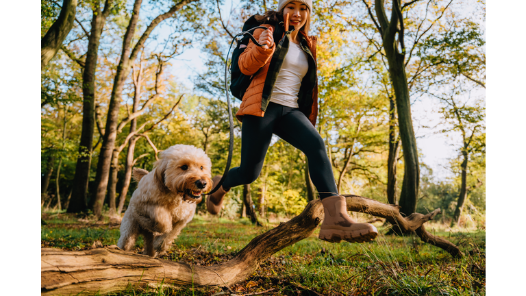 Young woman jumping over wooden trunk with her dog while exploring nature