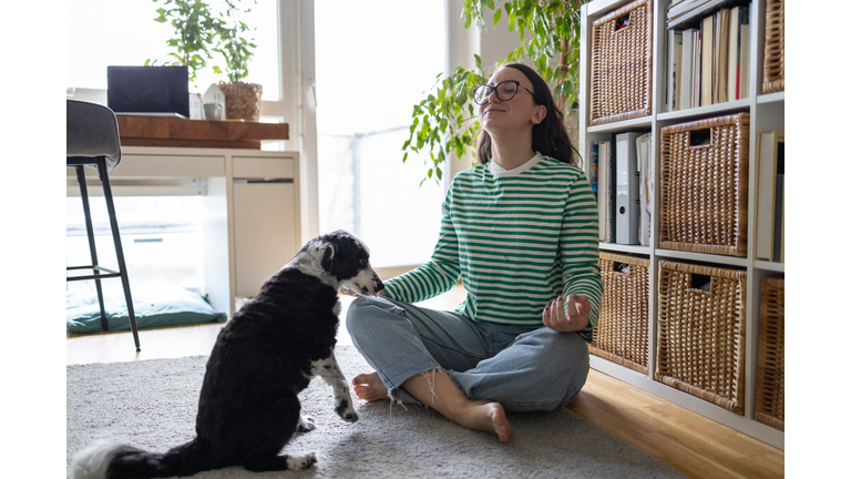 Young woman meditating at home in the morning, her curios dog sitting near her