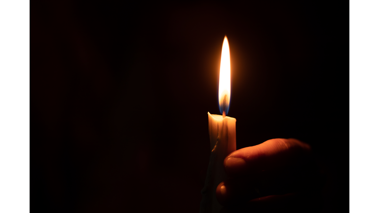 candle flame illuminates a female hand in a dark room