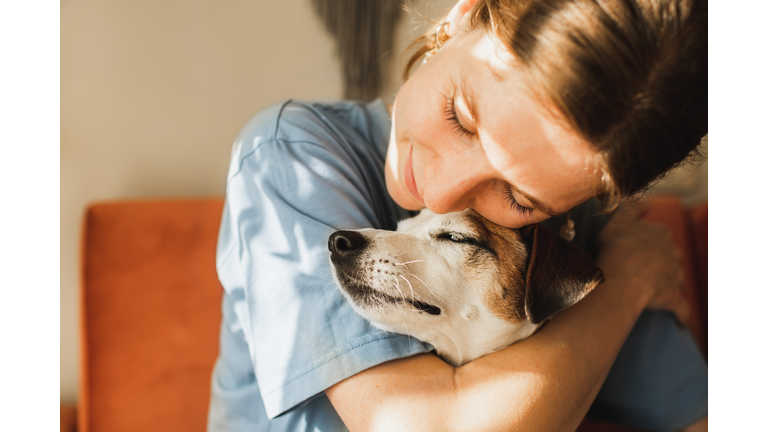 Cute young woman playing and hugging her jack russell terrier dog.