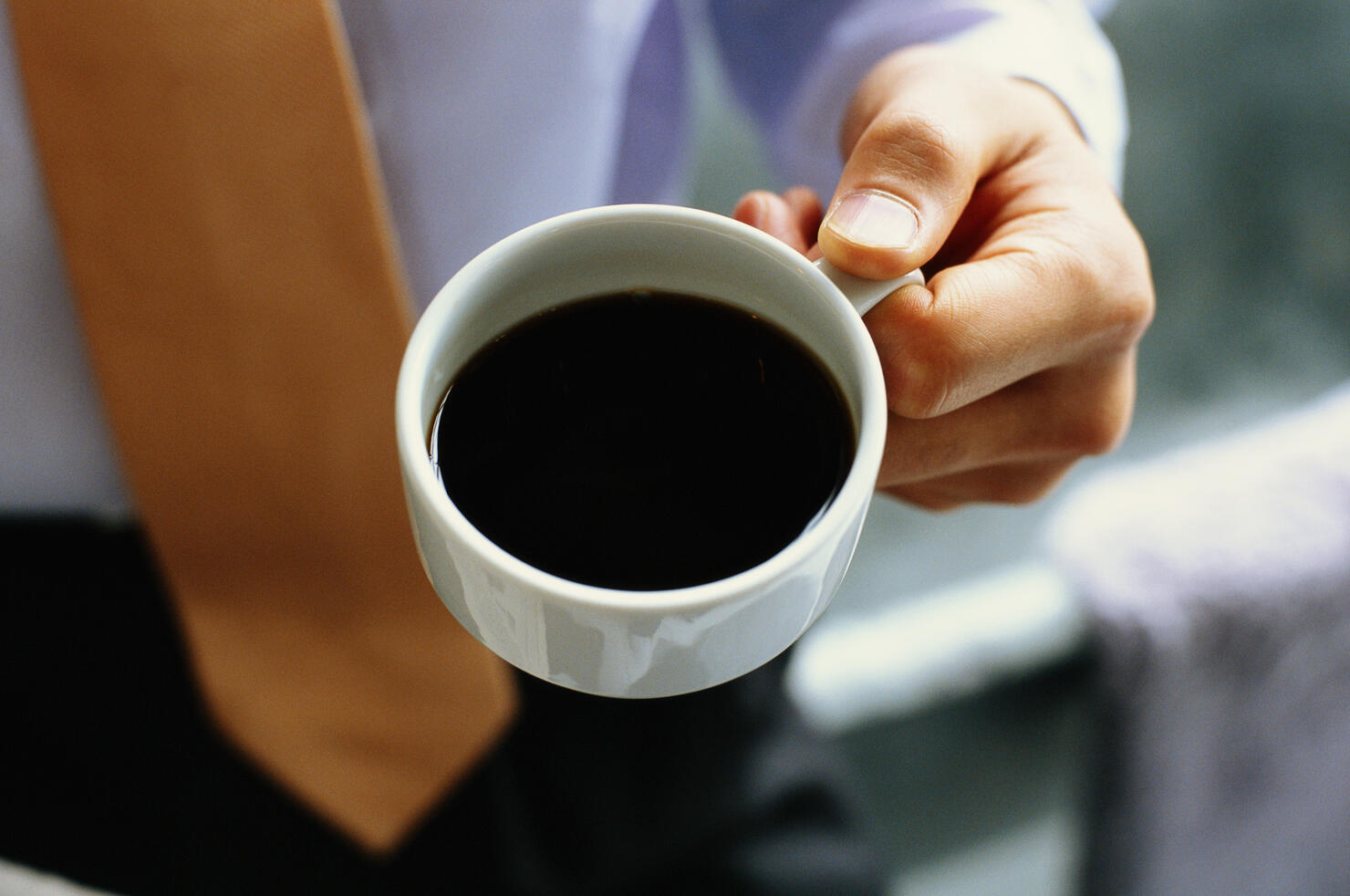 Businessman holding cup of black coffee, mid section, elevated view