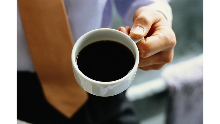 Businessman holding cup of black coffee, mid section, elevated view