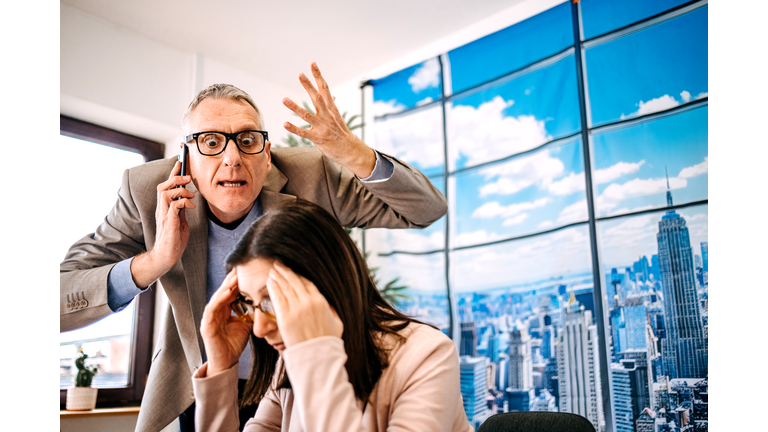 Male manager harassment female employee at work while having phone call on mobile phone