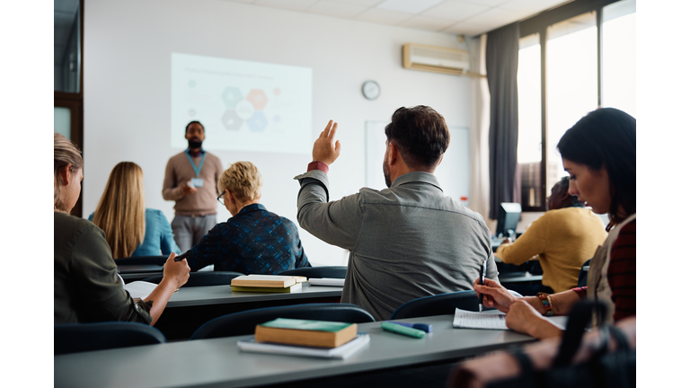 Back view of student raising his hand to answer teacher's question during education training class.