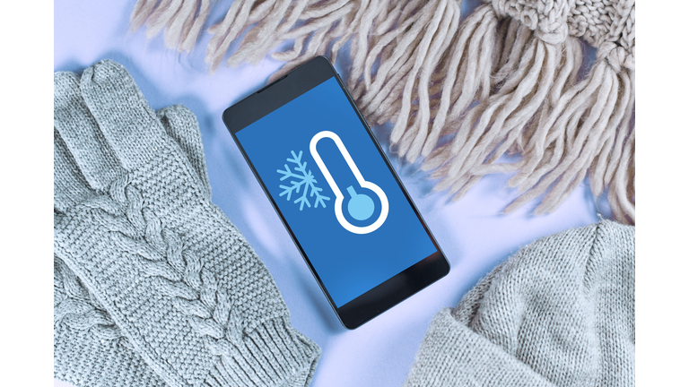 Concept for cold temperatures with snow and minus degrees with mobile phone showing weather forecast surrounded by warm clothes