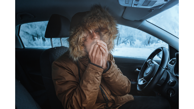 Man in down jacket tries to keep warm and not freeze in his stalled car in winter. The concept of a dangerous accident or heater failure in the cold season