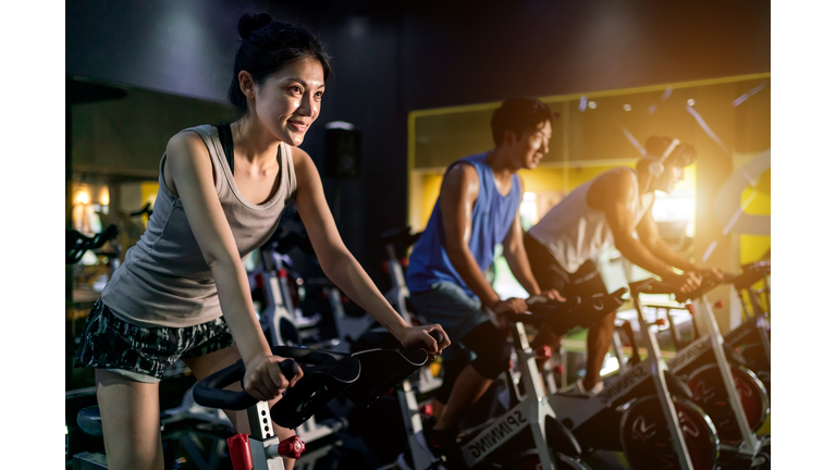Young people riding stationary bike during indoor cycling class in gym.