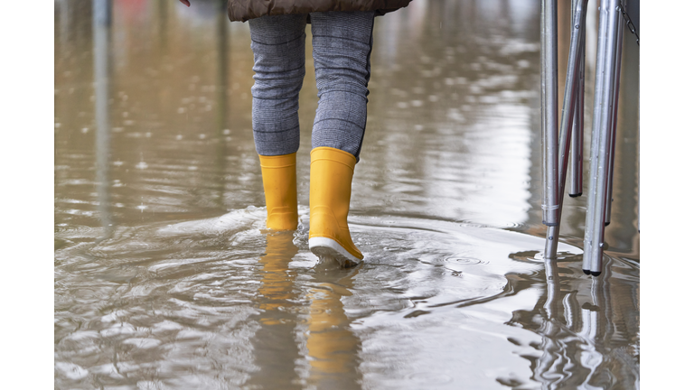 rear view of a woman walking on the sidewalk of the street flooded by the rain with yellow boots