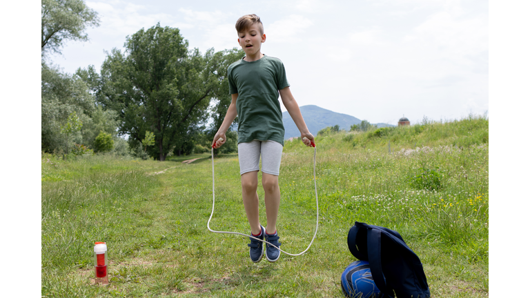 A boy is having fun jumping rope in the park, on a beautiful spring day.