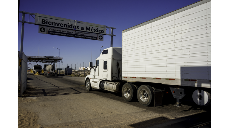 White Semi Truck Crossing the International Border Barrier Between the United States and Mexico Transporting Commercial Cargo