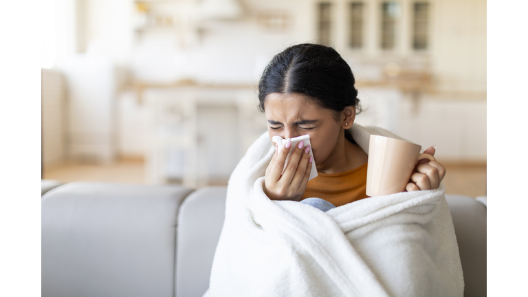 Cold And Flu Symptoms . Sick indian woman covered in blanket blowing nose