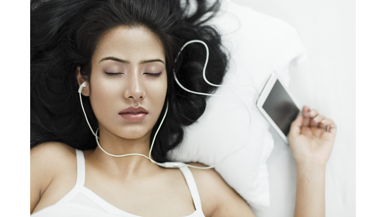 Young woman sleeping with smart phone and headphones on.