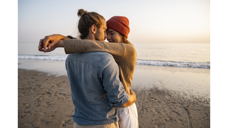 Young romantic couple standing face to face at beach against clear sky during sunset