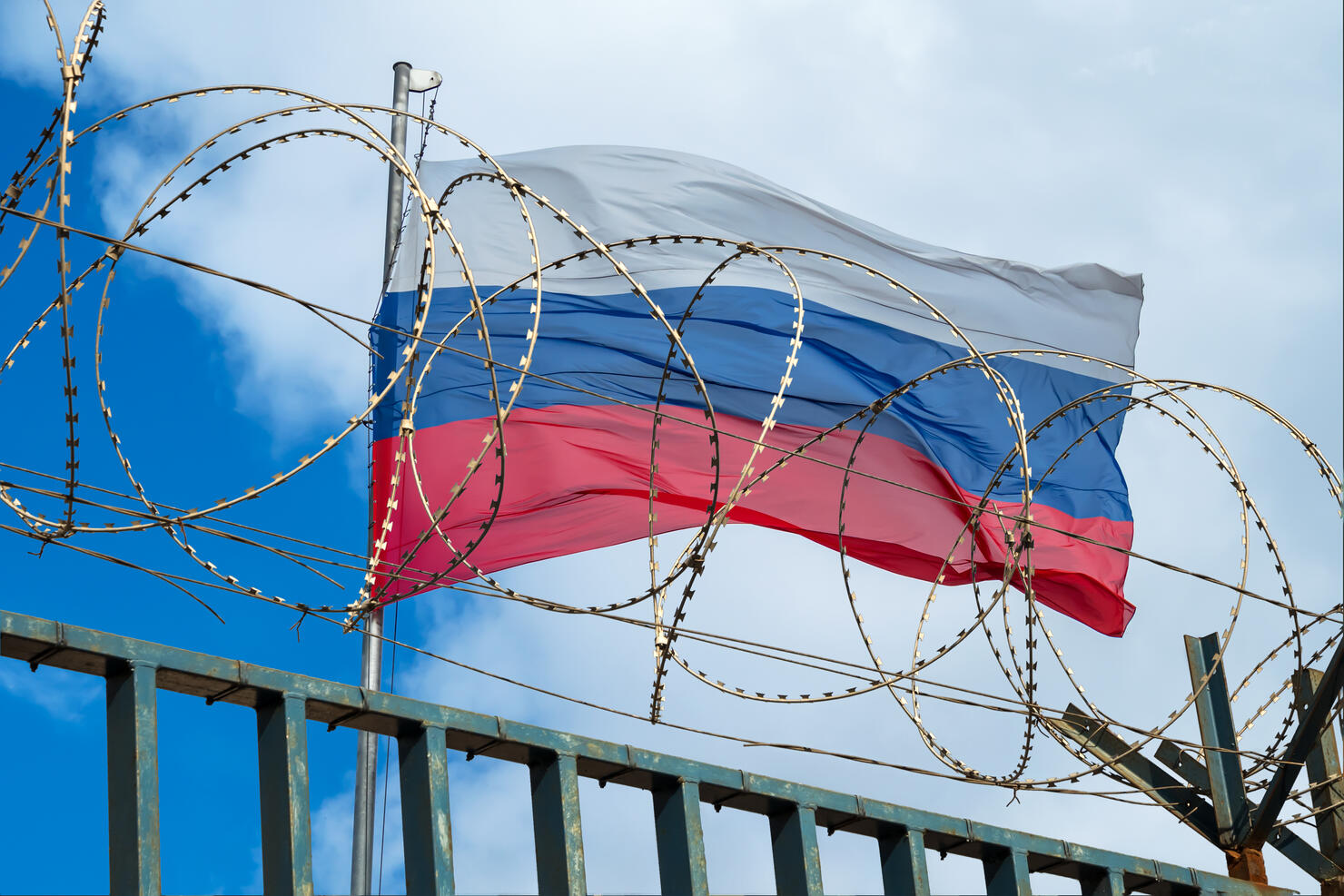 Russian flag behind barbed wire against cloudy sky