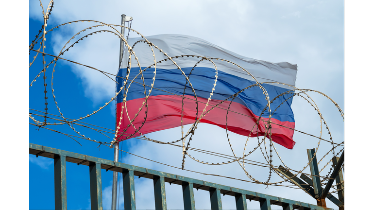Russian flag behind barbed wire against cloudy sky