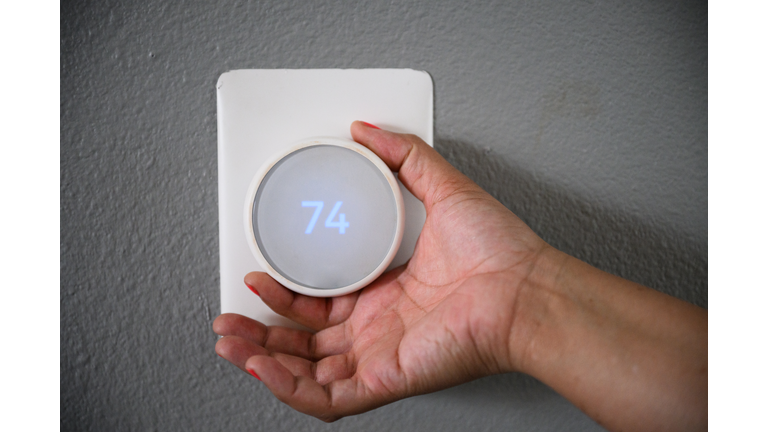 Close up of hand with nail varnish adjusting round thermostat knob against grey wall