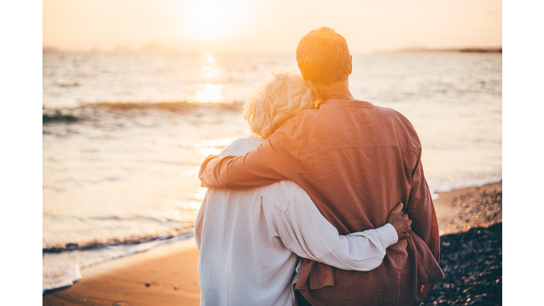 Happy mature couple enjoying beautiful sunset at the beach. Retirement Vacation Concept.