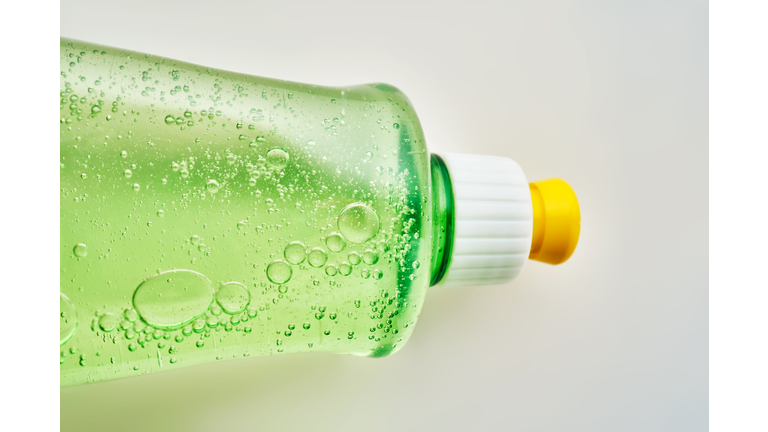 Green transparent bottle of dishwashing detergent with bubbles.