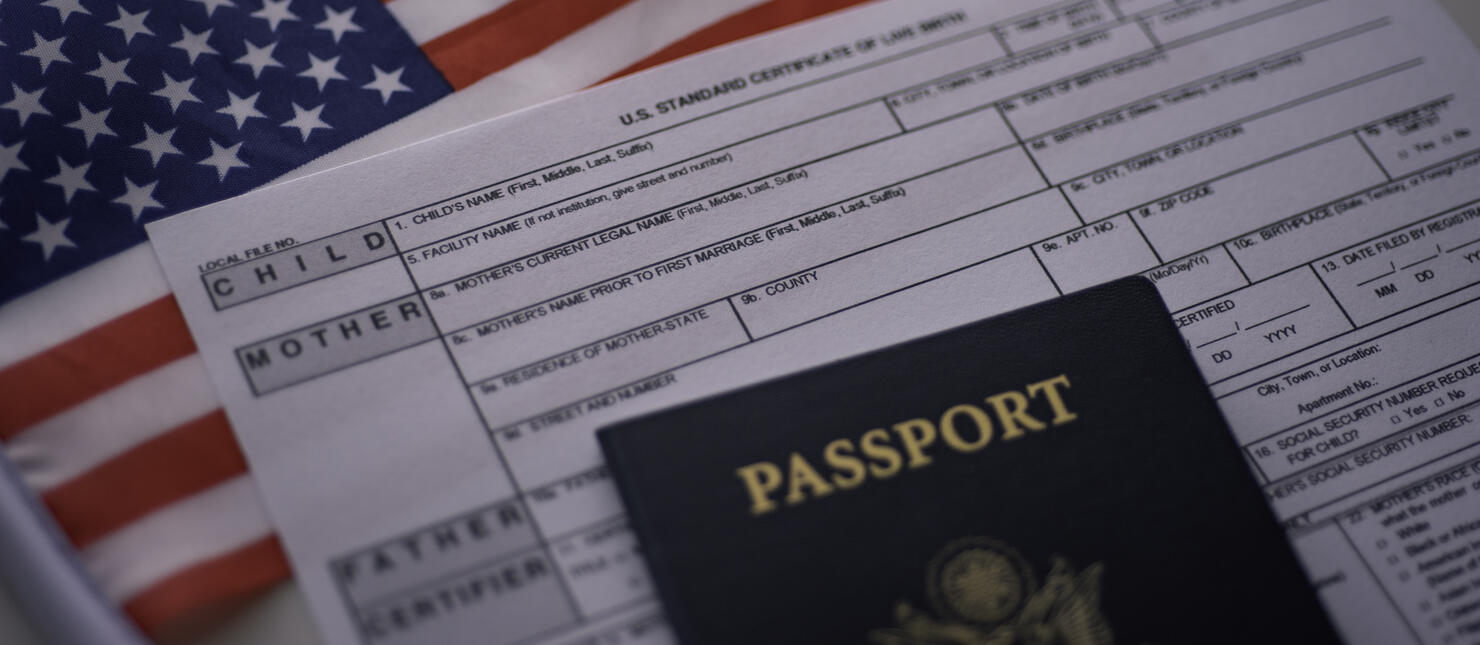 U.S. standard certificate of live birth application form next to American flag and Passport of USA. Wide photo.