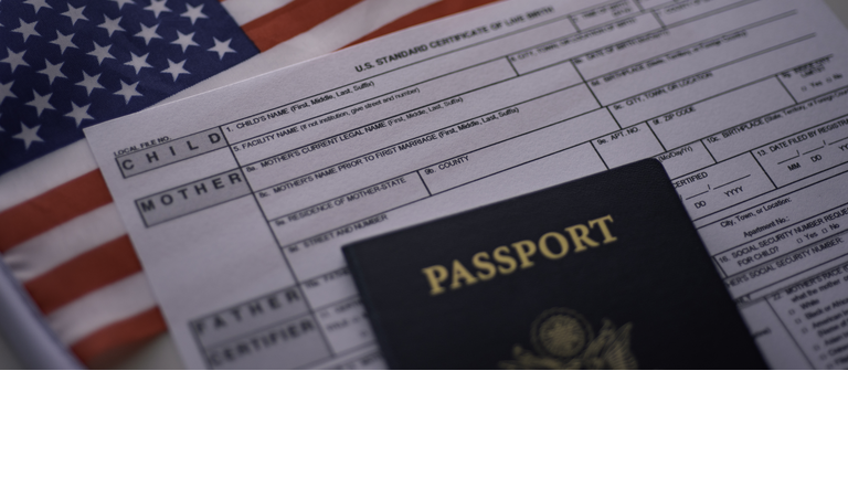 U.S. standard certificate of live birth application form next to American flag and Passport of USA. Wide photo.