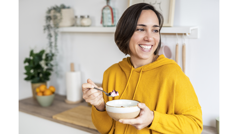 Woman enjoying healthy breakfast with yogurt and berries in kitchen