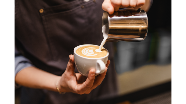 close up view of Young woman preparing a coffee by drawing a flower with milk