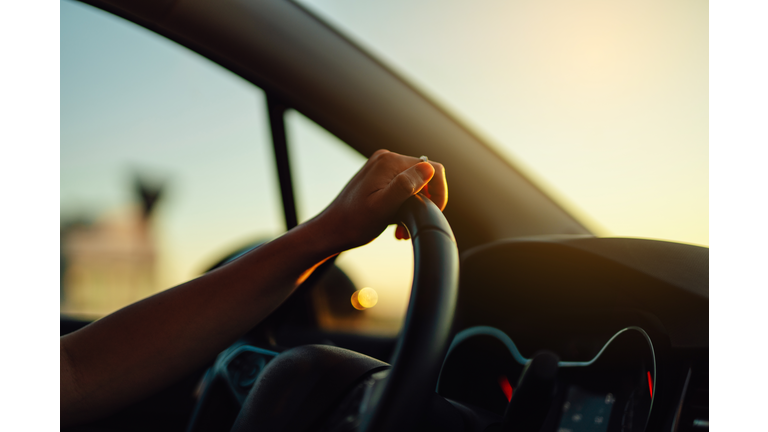 Female hand holding steering wheel in a car during a drive at sunset