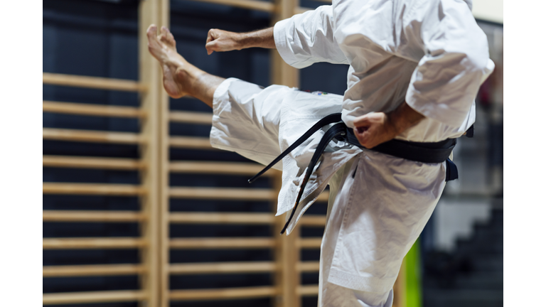 Mature man kicking while practicing karate in class