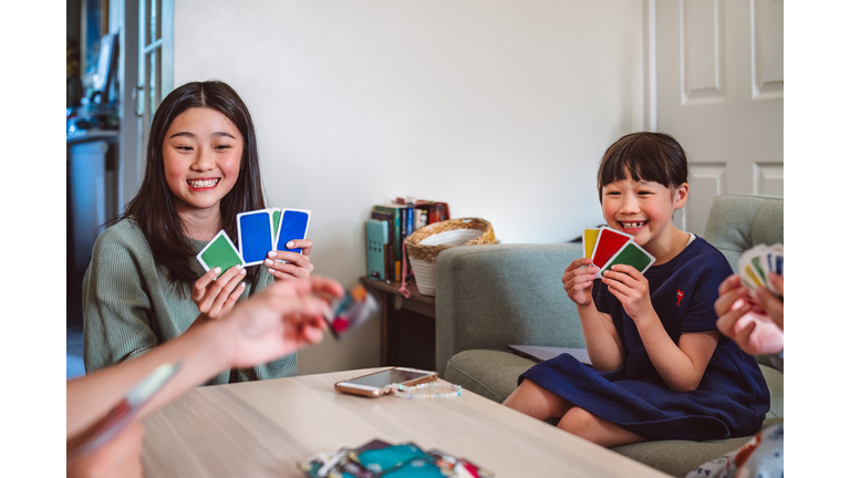 Young cheerful sister playing card game with family at home
