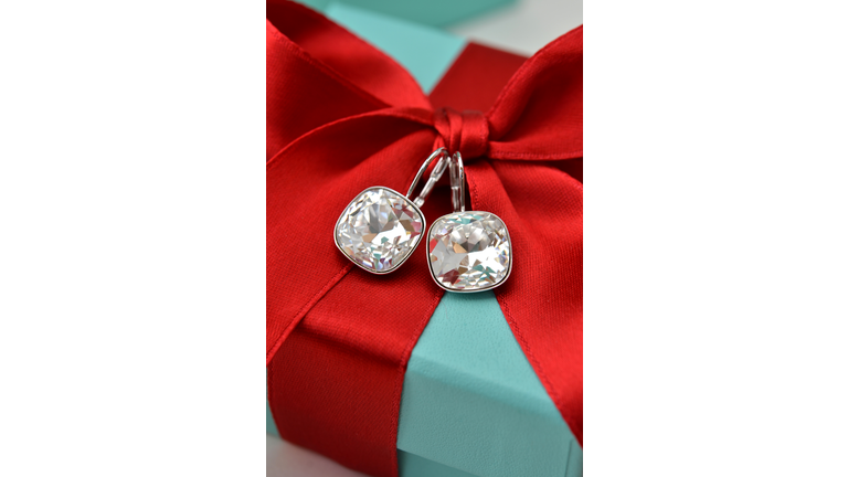 Diamond earrings attached to a red bow on a gift box