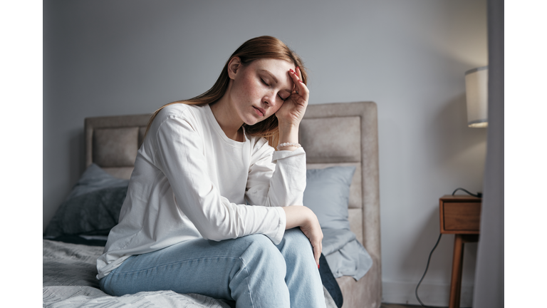 Morning Headache. Young woman sitting on bed with eyes closed touching head suffering from headache or migraine, feeling exhaustion