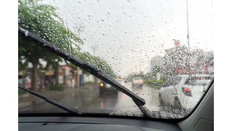 Car windshield with rain drops and frameless wiper blade closeup.